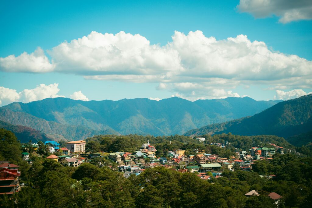 Breathtaking panoramic view of Baguio cityscape against majestic mountain backdrop under blue skies.